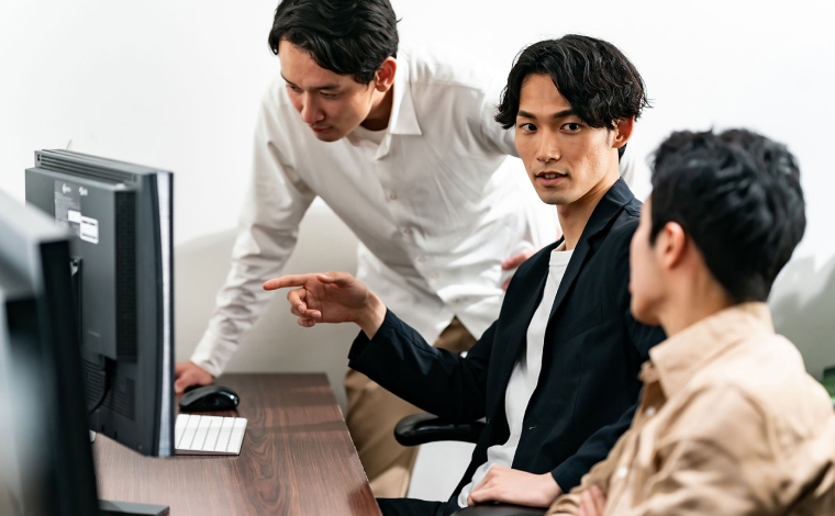 モニターを囲み、システム開発について話し合うエンジニアチーム